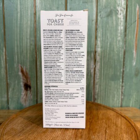A box of "Toast for Cheese" sits on a wooden surface against a green wooden background. The packaging displays ingredients, nutritional information, and product details in black text on a white label.