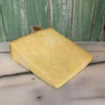 A wedge of Yoredale 250g cheese rests on a white marble surface with a rustic green wooden background.